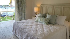 A bedroom with a bed, a nightstand, a lamp, and a view of a marina through a window.