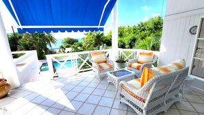 A covered patio with wicker furniture, a pool, and lush greenery in the background.