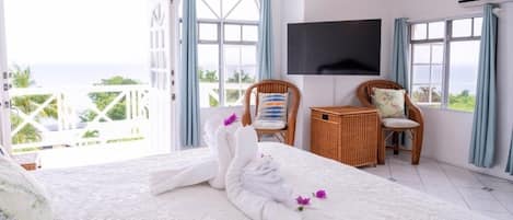 Une chambre d’hôtel avec un grand lit, un téléviseur fixé au mur, des fauteuils en osier et un balcon avec vue.