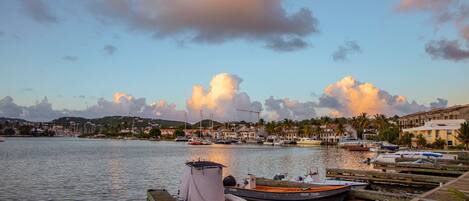 A marina with boats docked, a wooden dock, and a backdrop of buildings and hills.