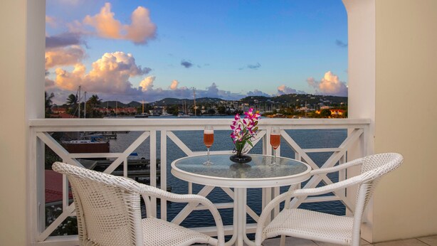 A balcony with white wicker chairs, a glass table, and a vase with flowers.