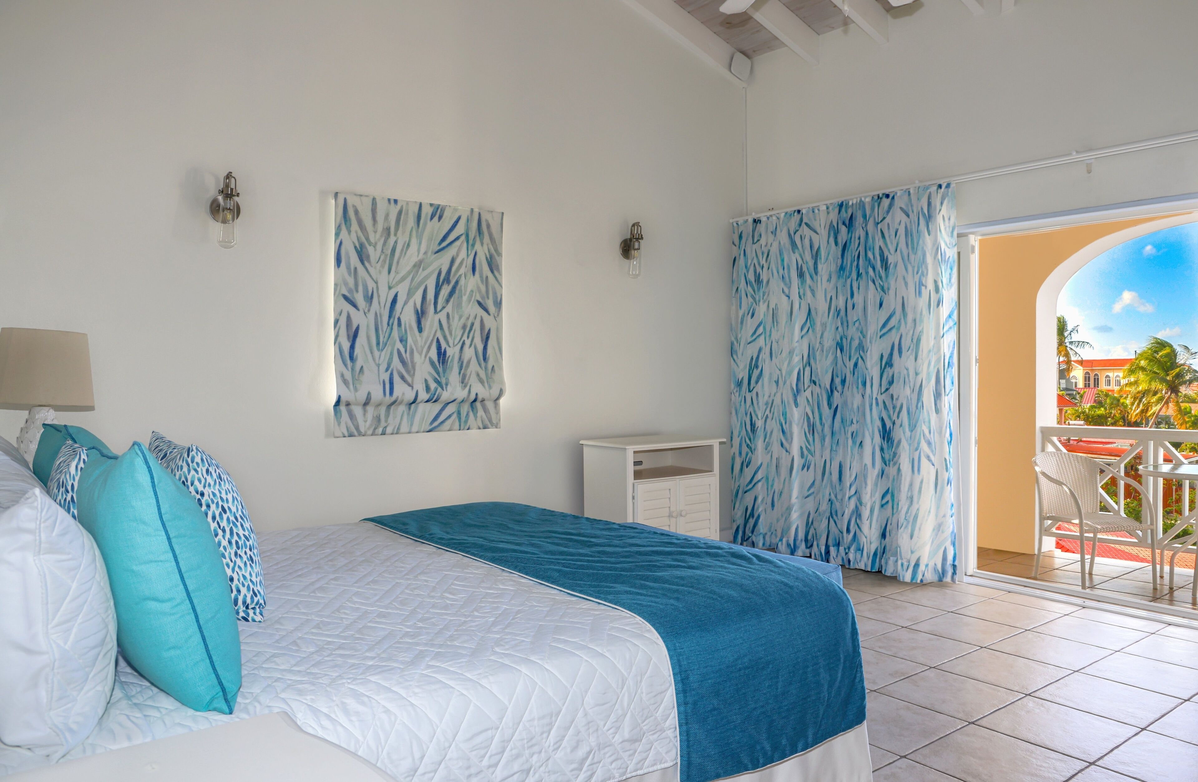 Un dormitorio con cama, mesita de noche, lámpara de pared y vistas al exterior.