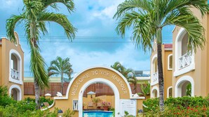 A resort entrance with a pool, palm trees, and a sign reading "WELCOME TO THE HARBOUR".