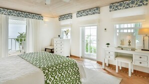 Een slaapkamer met een groot bed, een dressoir, een kaptafel met spiegel en een plafondventilator.