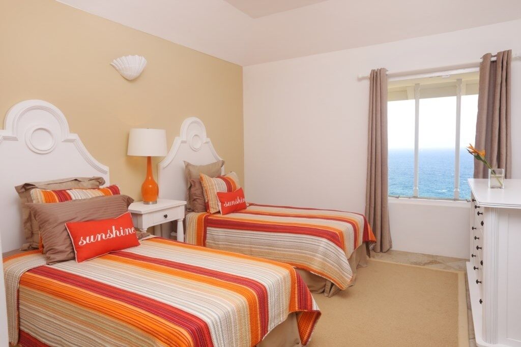 A hotel room with two beds, a nightstand, a lamp, a dresser, and a window with curtains.