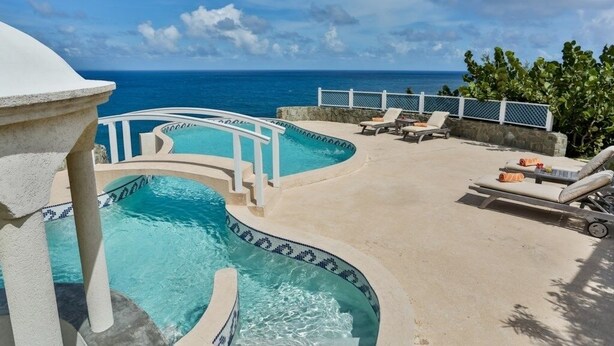 A pool area with multiple pools, lounge chairs, and a view of the ocean.