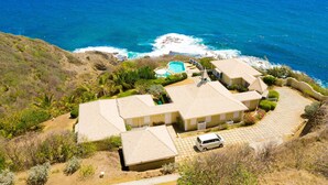A coastal property with a swimming pool, multiple houses, and a view of the ocean.