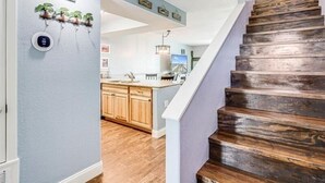 A modern kitchen with wooden cabinets, a central island, and a staircase with a rustic finish. - Sunset Breeze 3 Bedroom Condo by RedAwning (Rockport)