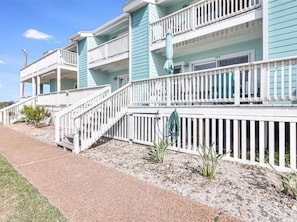 A row of beachfront cottages with white railings and a gravel walkway. - Sunset Breeze 3 Bedroom Condo by RedAwning (Rockport)