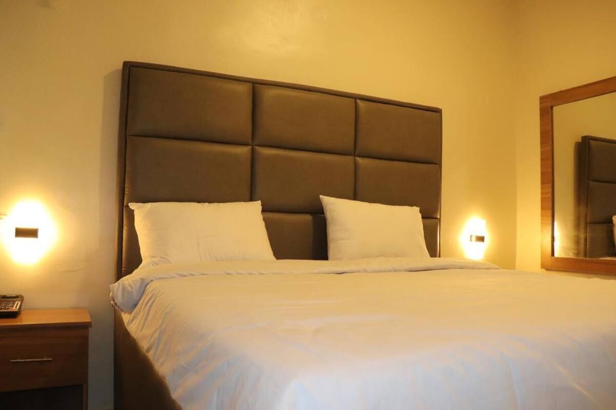 A hotel room with a large bed, two bedside lamps, a nightstand, and a mirror on the wall.