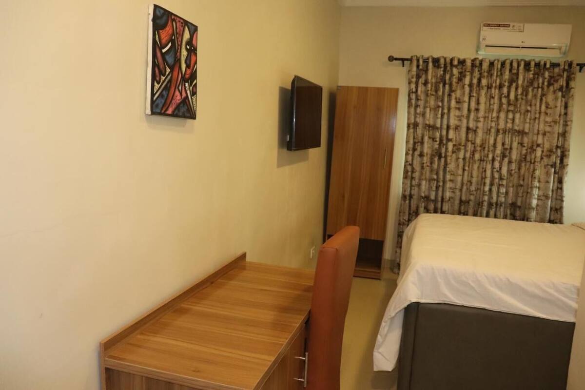 A hotel room with a bed, a desk, a chair, a television, and a wardrobe.