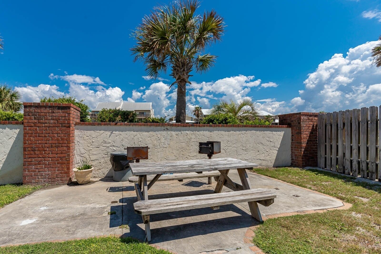 Une terrasse extérieure avec une table et des bancs en bois, un mur en briques et un palmier.