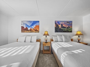 Habitación de hotel con dos camas, ropa de cama blanca, cabeceros de madera y dos mesitas de noche con lámparas.