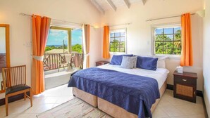 A bedroom with a large bed, two windows with curtains, a wooden chair, and a balcony with a view.