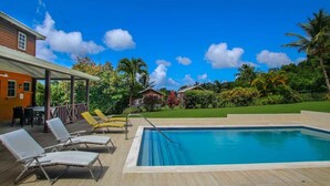 A swimming pool with lounge chairs, a covered patio, and a view of a tropical landscape.