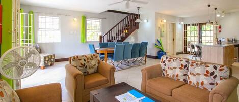 A living room with a sofa, armchairs, a coffee table, a fan, a staircase, and a dining area.