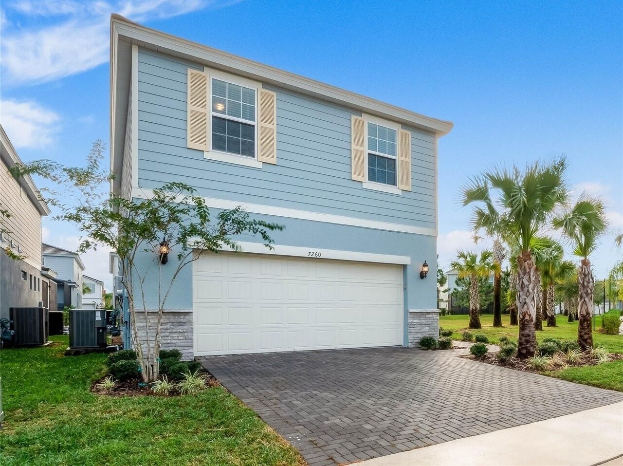 A two-story house with a garage, numbered 7260, surrounded by a well-maintained lawn and palm trees.