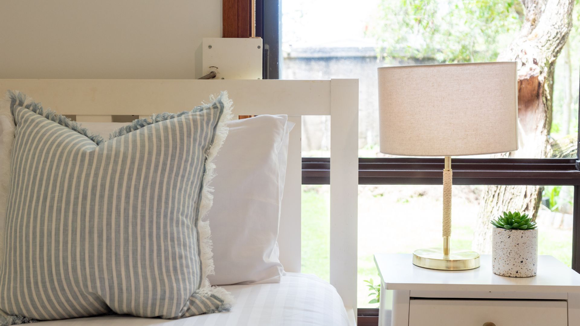 A bed with striped pillows, a bedside table with a lamp, and a small plant.
