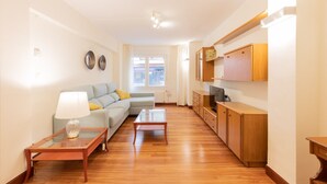Een woonkamer met een bank, twee salontafels, een televisie, houten kasten en een raam met gordijnen.