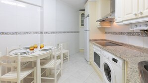 Een compacte keuken met witte kastjes, een ingebouwde wasmachine en een eethoek met een ronde tafel en stoelen.