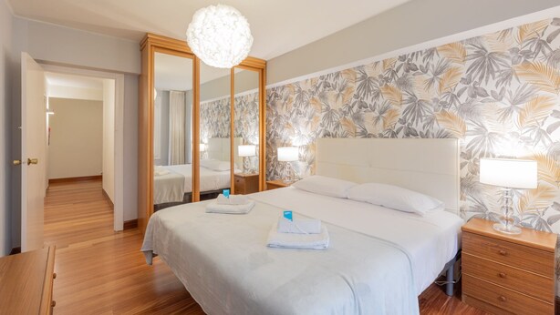 Hotelkamer met een groot bed, een houten garderobe, een spiegel, een nachtkastje met een lamp en tropische behang.