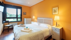 Habitación de hotel con cama, mesitas de noche, una silla, ventana con vistas y un cuadro en la pared.