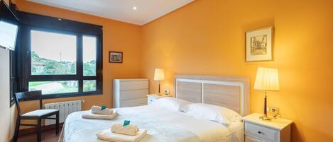 A hotel room with a bed, bedside tables, a chair, a window with a view, and a picture on the wall.