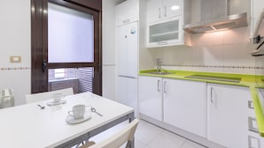 Una cocina compacta con armarios blancos, una encimera verde y una ventana con persianas.