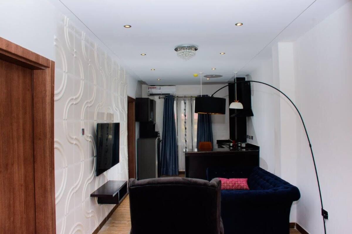 Un salon moderne avec un téléviseur à écran plat fixé au mur, un canapé bleu foncé, un meuble en bois et une cloison en verre.