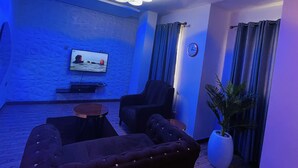 A modern living room with a flat-screen TV, two armchairs, a coffee table, and a potted plant. - James Court Hotel & Luxury Apartments (Lekki)