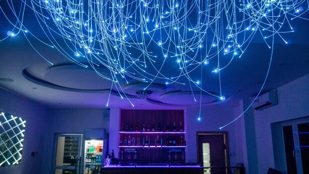 A bar area with a ceiling adorned with blue light strings, a bar counter, and shelves stocked with bottles. - James Court Hotel & Luxury Apartments (Lekki)