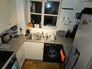 A compact kitchen with a dishwasher, a sink, a window, and a washing machine.