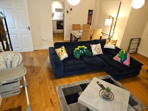 A living room with a dark blue sectional sofa, a small table with a plant, and a grey patterned rug.