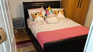 A bedroom with a wooden bed, a nightstand, a wardrobe, and a window with blinds.