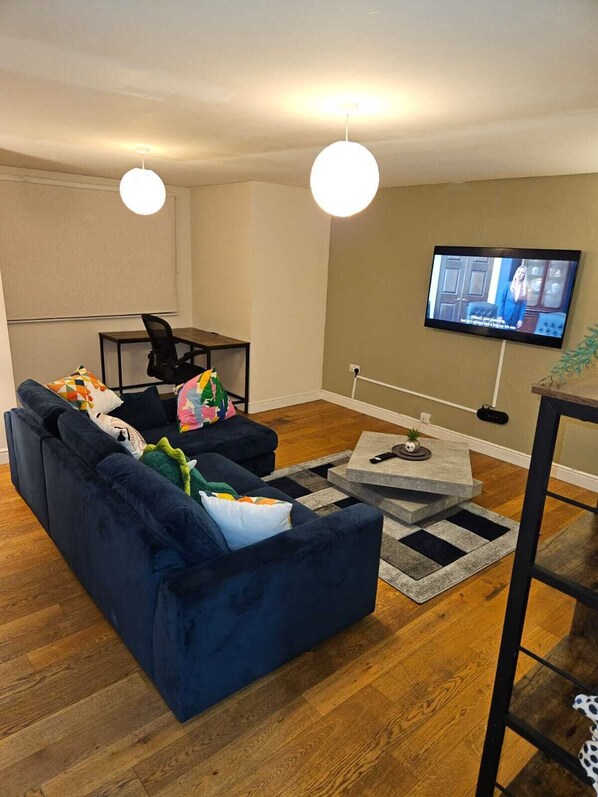 A living room with a dark blue sofa, a small table, and a television on the wall.