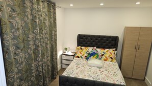 A bedroom with a bed, a nightstand, a dresser, and a curtain with a leaf pattern. - 1 Bed Flat - Sleeps 2 - Parking - Garden (London)