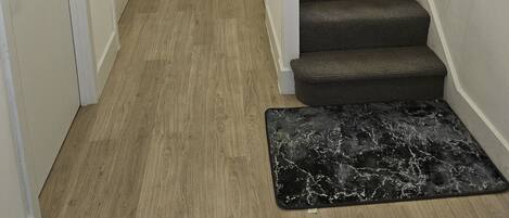 A staircase with a dark carpeted handrail and a black marble mat at the bottom.