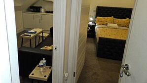 A compact hotel room with a kitchenette, a bed with patterned bedding, a small table with a remote control, and a water bottle on a side table. - 1 Bed Flat - Sleeps 2 - Pets - Garden - Parking (London)
