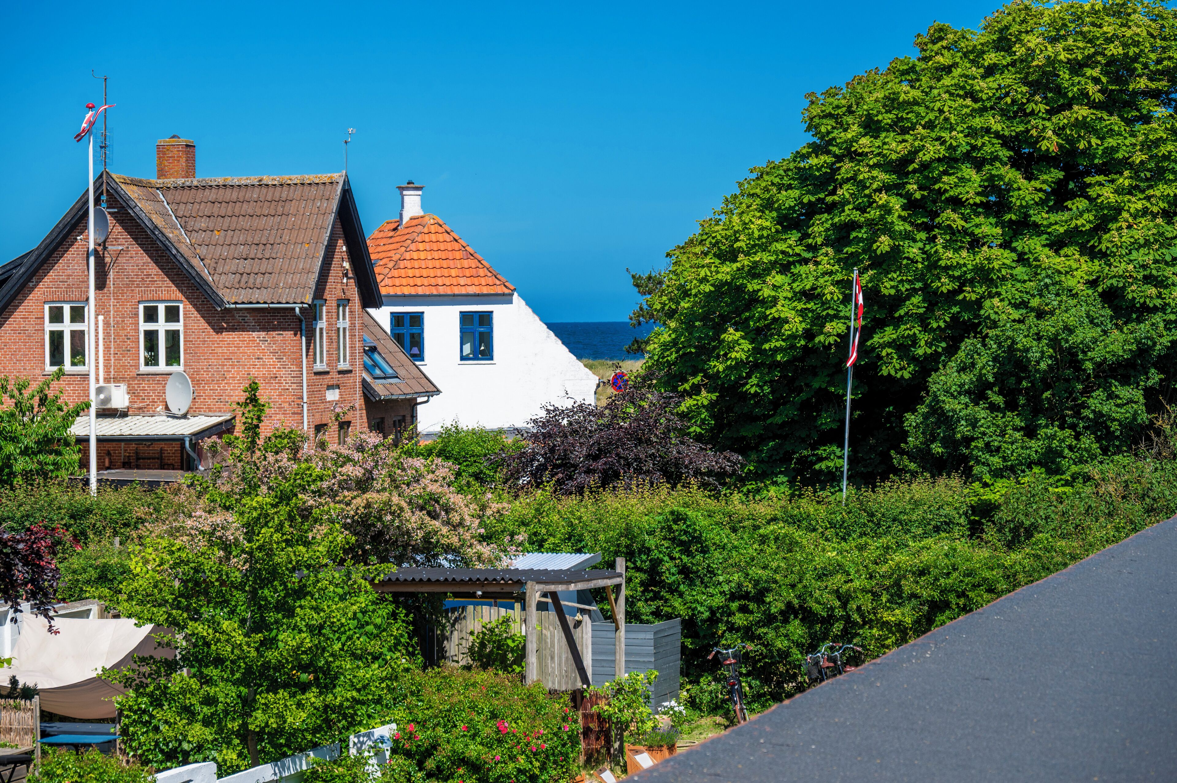 A coastal residential area with houses, a clear sky, and a view of the sea.