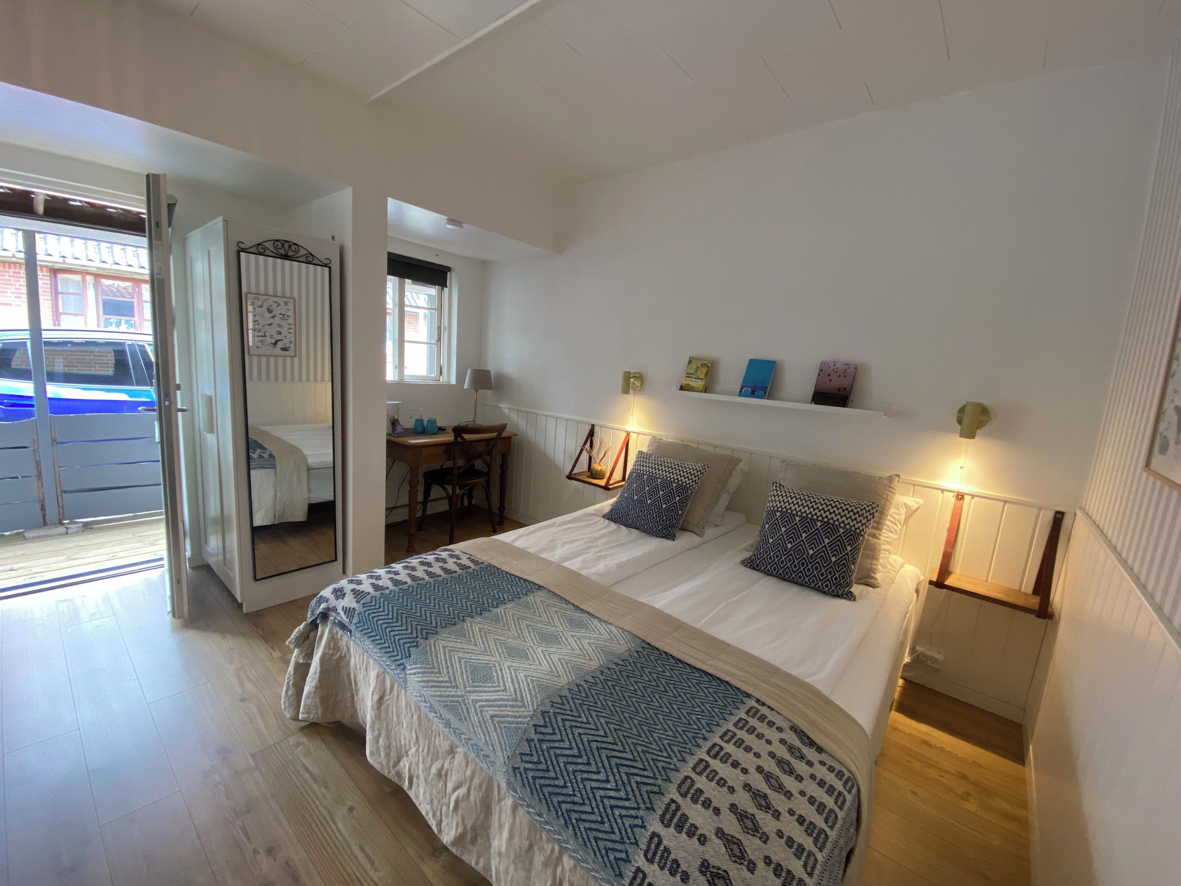 A bedroom with a bed, a desk, and a chair. There is a door leading to another room.