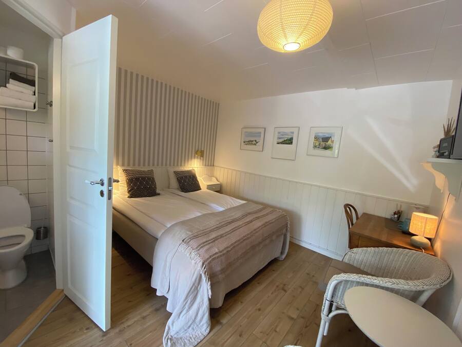 Un dormitorio con cama, mesita de noche, silla, lámpara y estante en la pared.