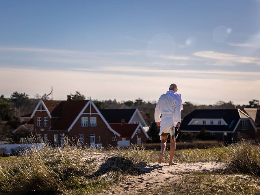 A person walking on a sandy path with houses in the background.