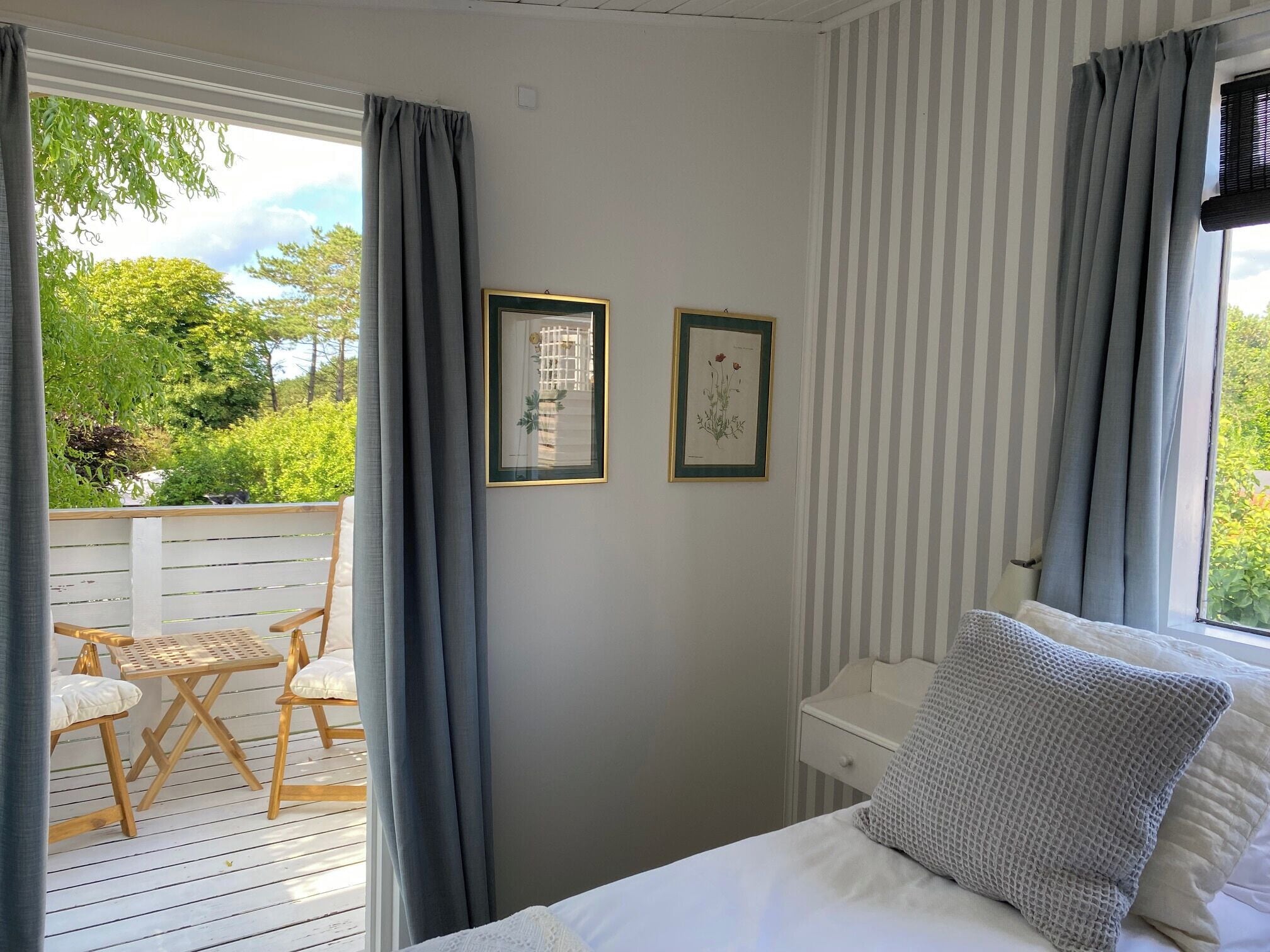 A bedroom with a bed, a nightstand, and two framed botanical prints on the wall.