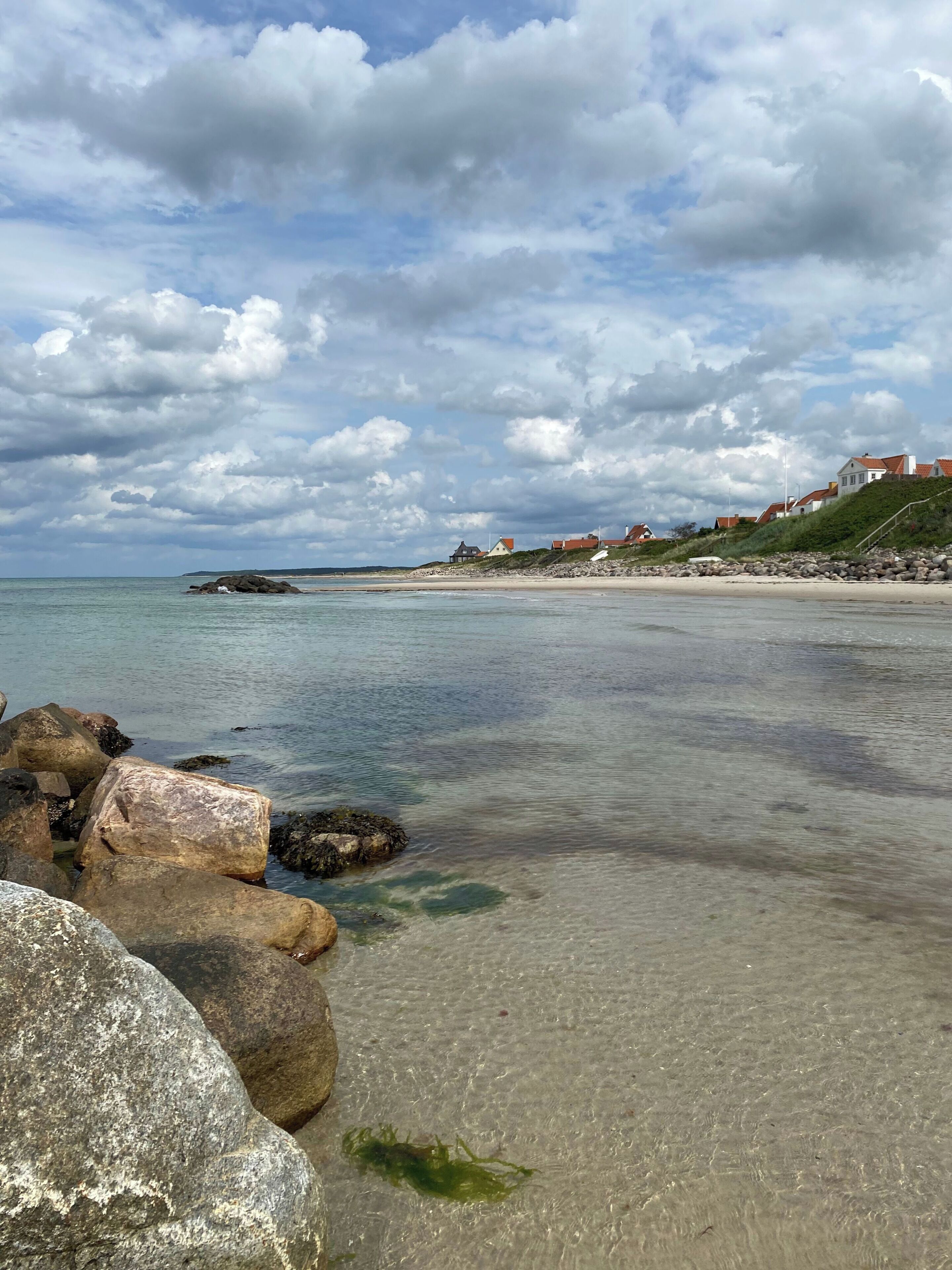 A coastal landscape with clear water, rocks, and houses on a hillside.