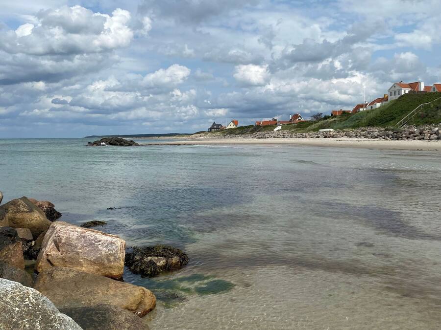 A coastal landscape with clear water, rocks, and houses on a hillside.