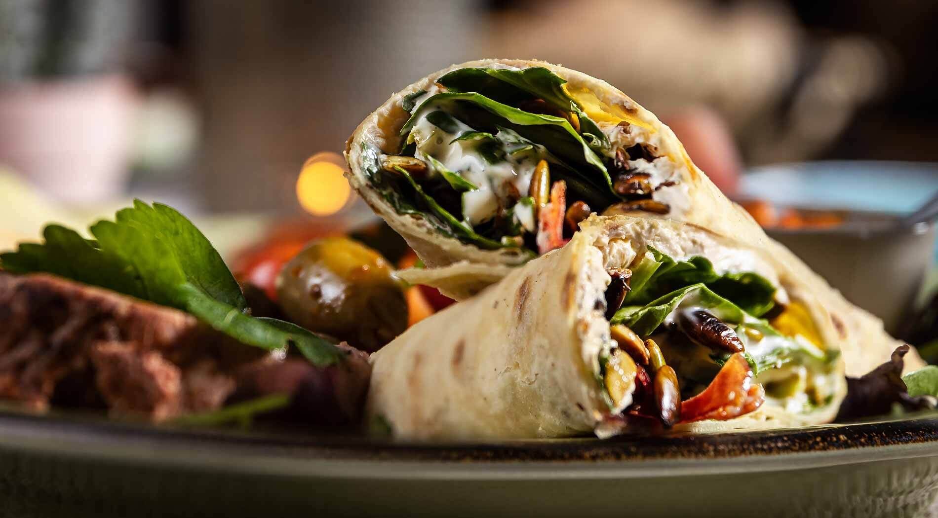A wrap with greens, cheese, and a creamy sauce, served on a plate with a side salad.