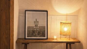 A framed sign with 'PUBLIC ACCESS TO BEACH' text, a table with a candle and a lamp, and a large pot on the floor.