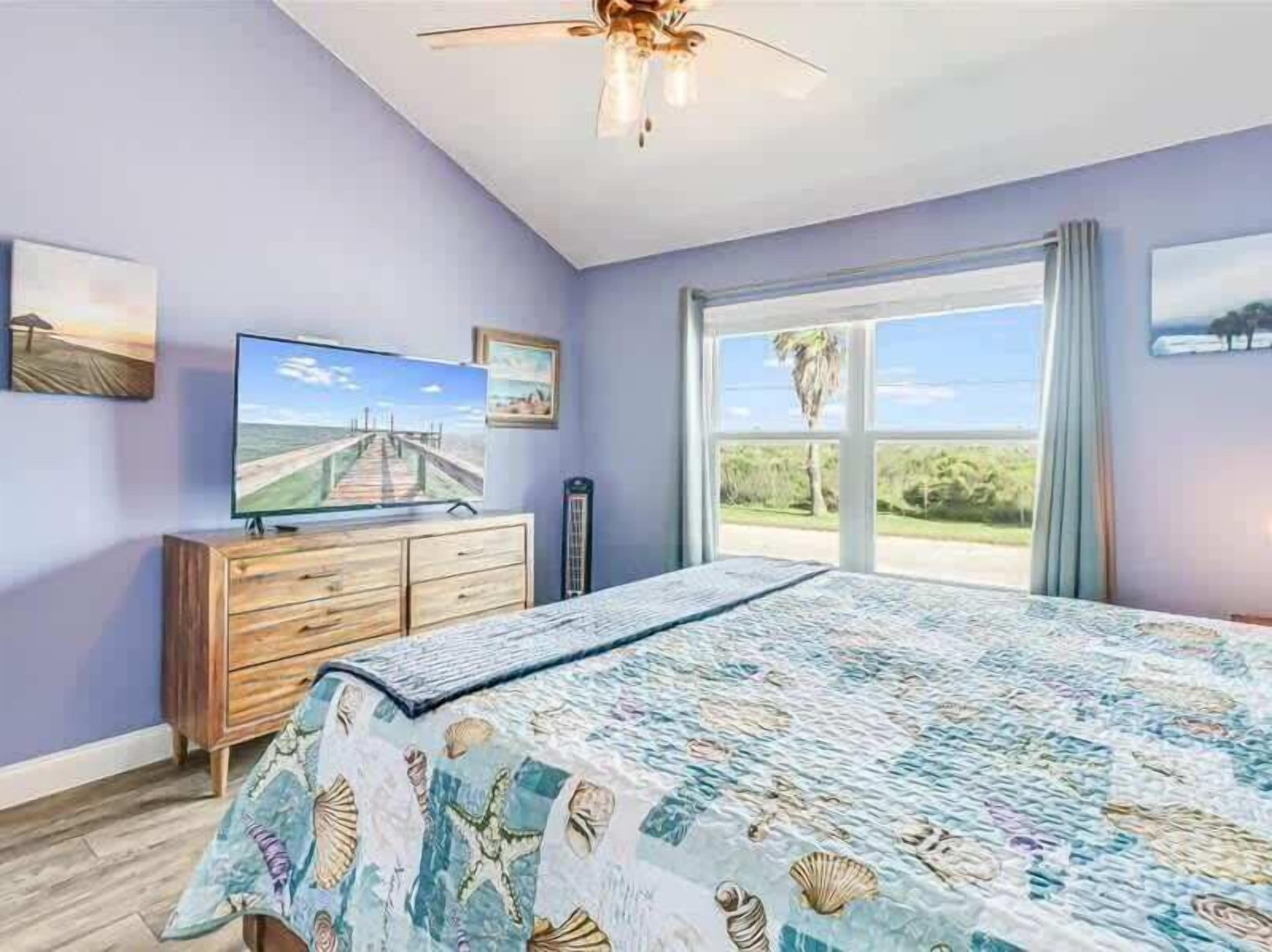 Un dormitorio con una cama grande, televisión, cómoda de madera y vistas al exterior.