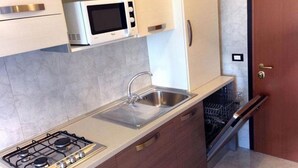 A compact kitchen with a gas stove, a microwave, a sink, and a dishwasher. - Spend Your Holiday in our Beautiful Flat-beahost (San Michele al Tagliamento)