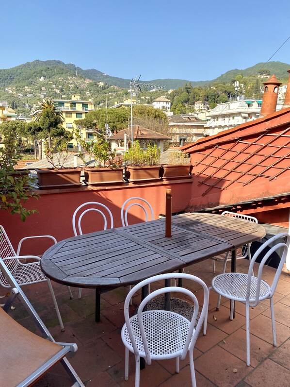 Une terrasse avec une table et des chaises, donnant sur une colline parsemée de bâtiments.